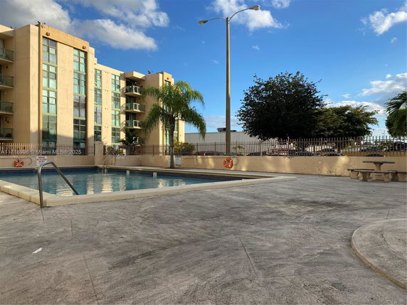 Outdoor swimming pool area with a multi-story building in the background.