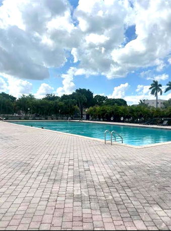 Outdoor swimming pool with surrounding trees and a paved deck.