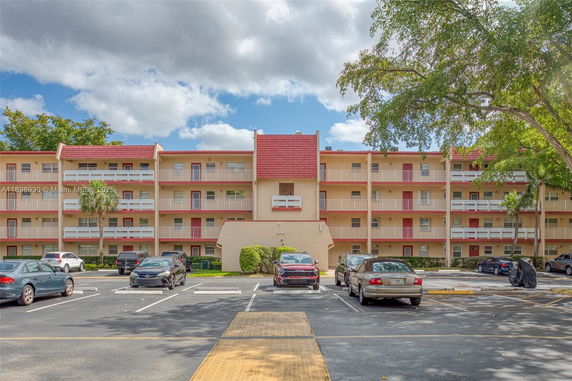 Front view of a four-story apartment building with balconies and parking spaces.