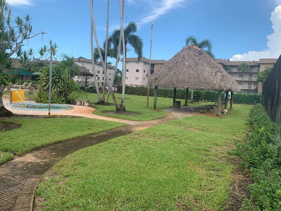 Outdoor view of a swimming pool with a thatched pavilion and surrounding lawn.
