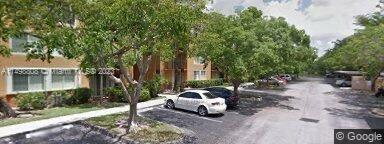 Outdoor parking area with multiple cars and trees near a building.