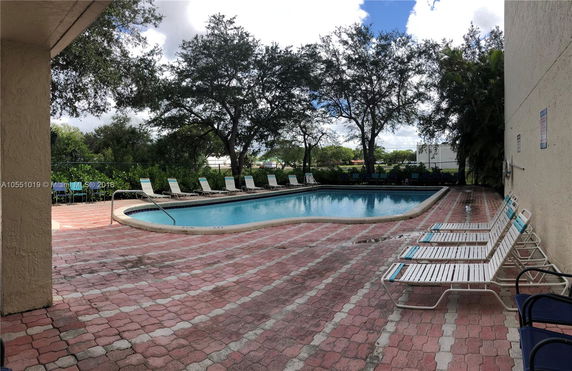Outdoor swimming pool area with lounge chairs and a surrounding fence.