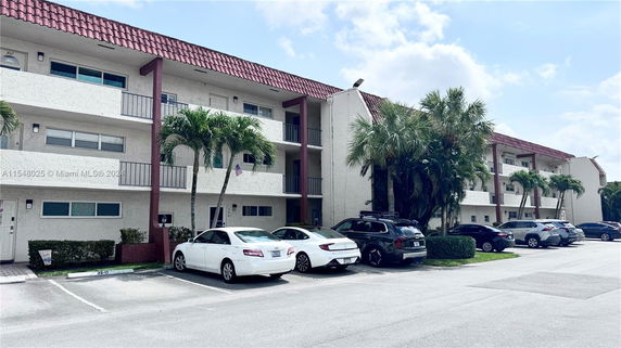 Front view of a multi-story building with balconies and parked cars.