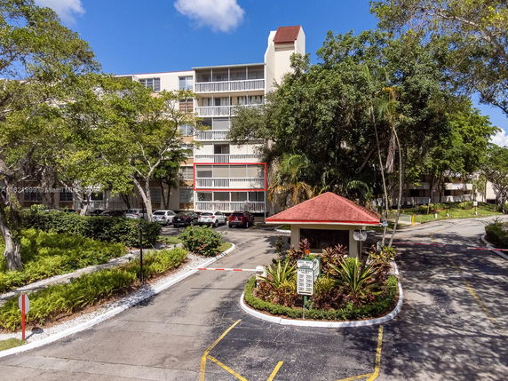 Front view of a multi-story residential building with balconies and a parking area in front.