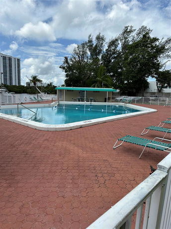 Outdoor swimming pool area with lounge chairs and a small building nearby.