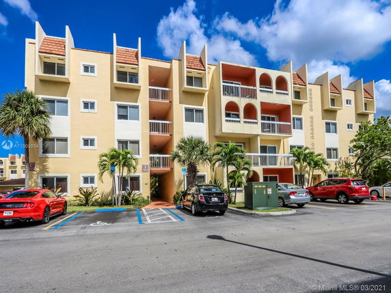 Front view of a four-story apartment building with balconies and parking spaces.