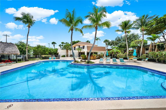 Outdoor swimming pool surrounded by palm trees and lounge chairs.