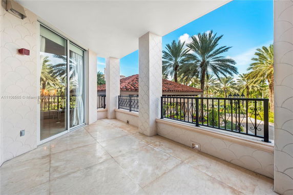 Covered outdoor patio area with decorative columns and railings, overlooking palm trees and a red-tiled roof.