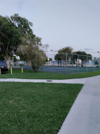 Outdoor tennis court surrounded by trees and grass.