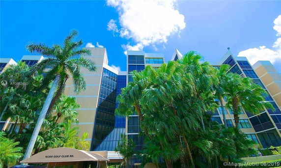Front view of a multi-story building with large glass windows and palm trees in front.