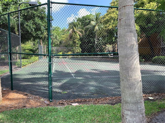 View of a fenced tennis court with surrounding trees.