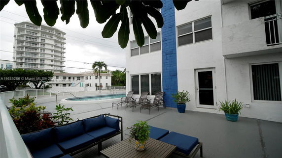 View of a multi-story residential building with a pool area and outdoor seating at the front.