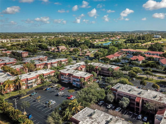Wide aerial view of residential buildings with parking areas and greenery.