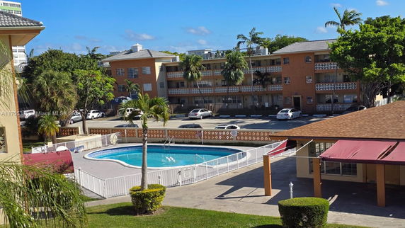 Outdoor swimming pool with surrounding buildings and parking area.
