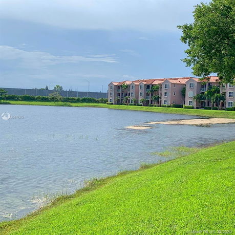View of apartment buildings by a lake with green grass.