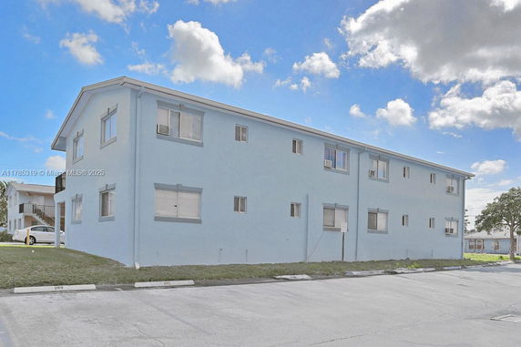 Side view of a two-story blue building with multiple windows and a parking area.