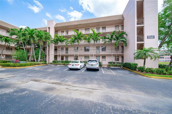 Front view of a four-story apartment building with a parking area and two cars parked in front.