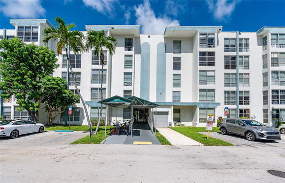 Front view of a multi-story residential building with a covered entrance and surrounding palm trees.