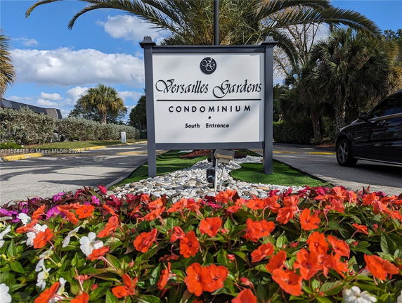 Entrance sign of Versailles Gardens Condominium with colorful flowers in the foreground.