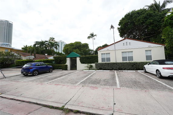 Outdoor parking area in front of a single-story house with hedges.