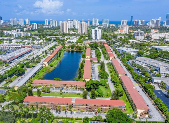 Aerial view of a cityscape featuring multiple residential buildings with red roofs, surrounding a central lake.
