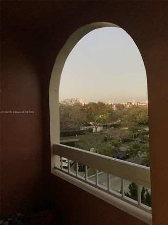 View through an arched opening showing trees and buildings in the distance.