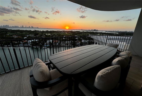 Balcony with outdoor dining set overlooking cityscape and waterfront at sunset.