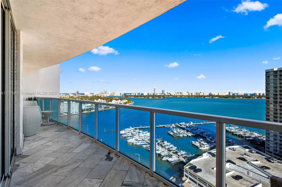 Balcony with glass railing overlooking a marina and city skyline.