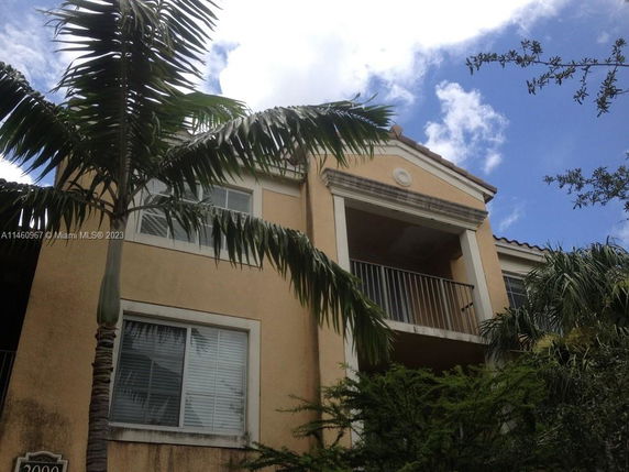 Front view of a multi-story house with a balcony and palm trees.