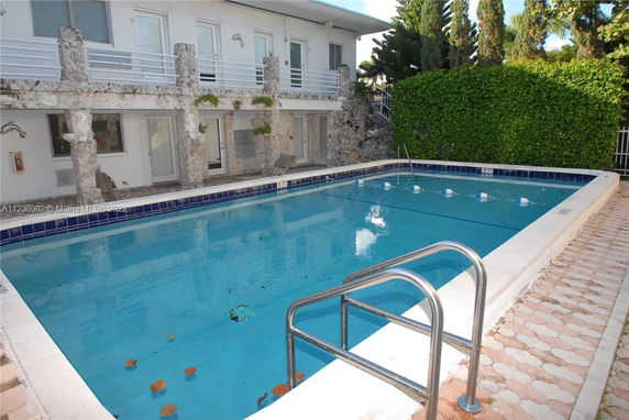 Outdoor swimming pool adjacent to a two-story building with balconies and stone columns.