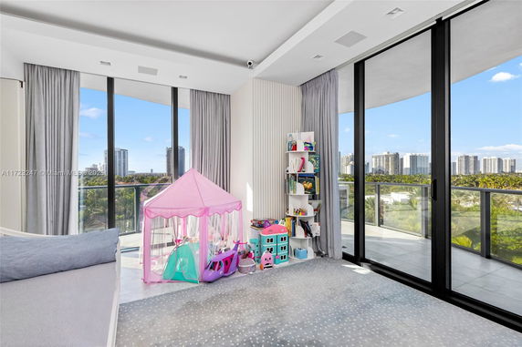 Indoor play area with children's tent, toys, and a bookshelf, featuring large windows with a view outside.