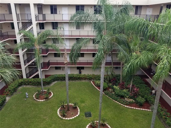 Outdoor view of a multi-story apartment building with balconies overlooking a landscaped garden with palm trees.