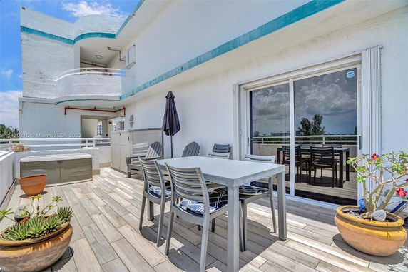 Rooftop patio with a dining table, chairs, and potted plants on a deck, adjacent to a white building.