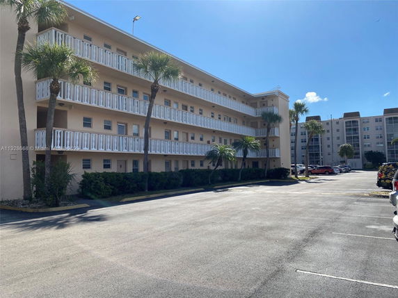 Front view of a multi-story building with white balconies and palm trees in front.