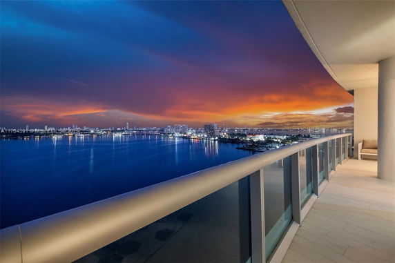 Balcony view overlooking a body of water with cityscape and colorful sunset.