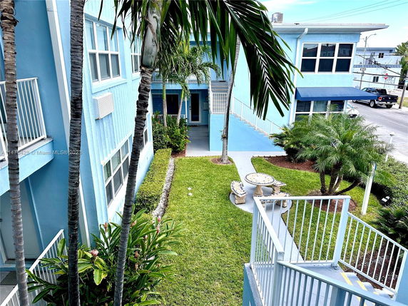 Front view of a multistory blue building with a stairway entrance and landscaped garden.