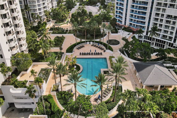 Aerial view of a swimming pool surrounded by palm trees and residential buildings.