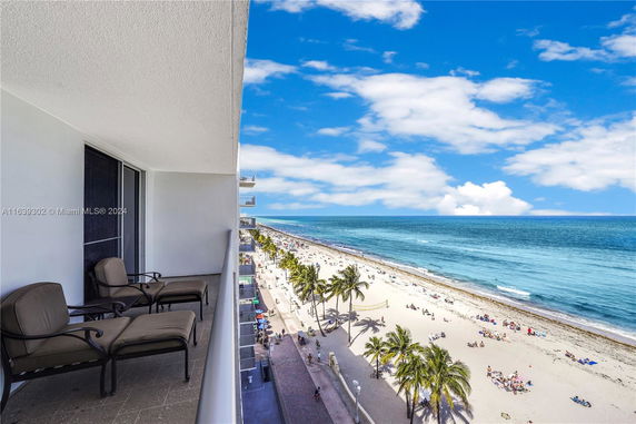 Panoramic view from a building balcony overlooking a sandy beach and ocean.