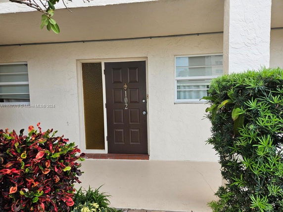 Front view of an apartment entrance with a brown door numbered 102 and flanked by two windows.