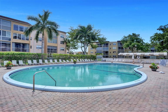 Outdoor swimming pool area with surrounding buildings and palm trees.