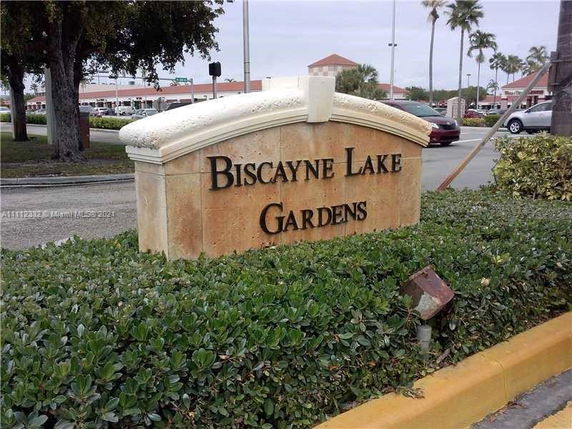 Sign for Biscayne Lake Gardens with greenery and road in the background.