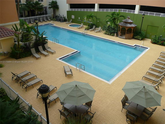 Rooftop with a swimming pool and lounge chairs, surrounded by a fence and greenery.