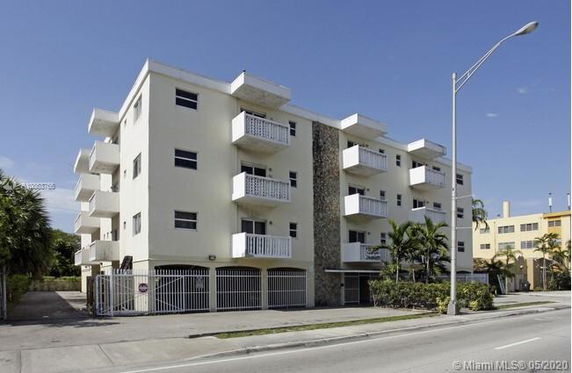 Front view of a multi-story apartment building with balconies and gated parking.