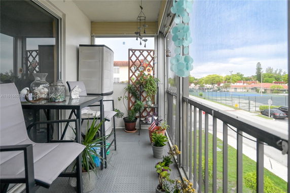 View from a balcony with potted plants and outdoor seating overlooking a tennis court.