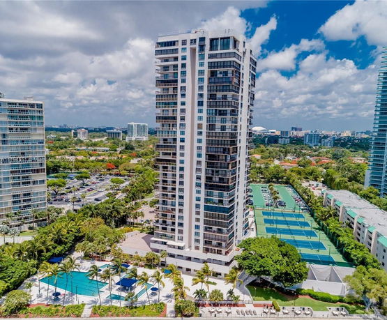 Aerial view of a tall residential building with tennis courts and a swimming pool in a landscaped area.