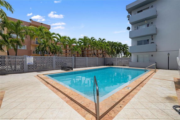 Outdoor area with a swimming pool surrounded by a fence and adjacent buildings.