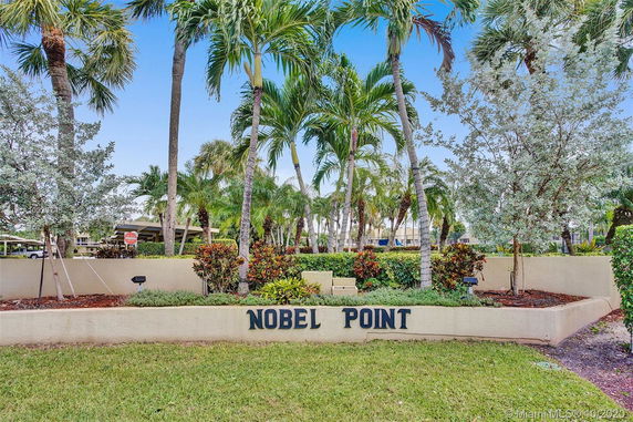 Outdoor view of a landscaped area with palm trees and a sign saying 'Nobel Point'.