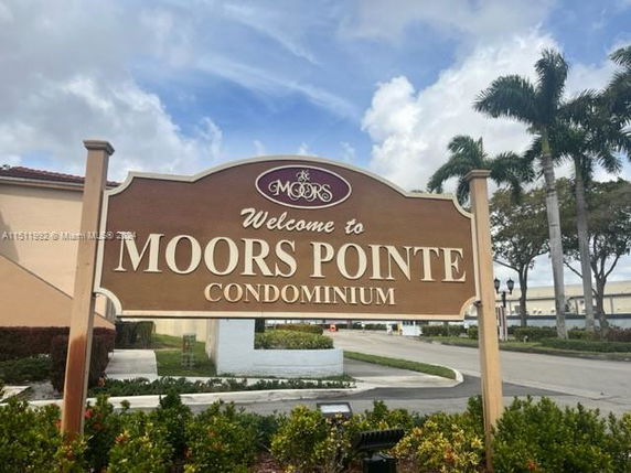 Sign for Moors Pointe Condominium with palm trees and parking area in the background.