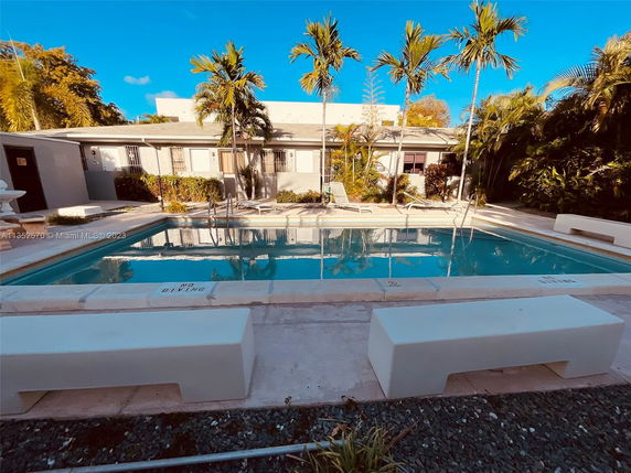 Outdoor swimming pool area with surrounding seating and palm trees.