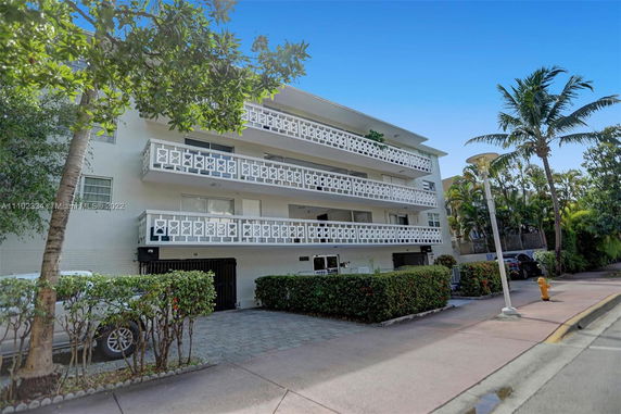 Front view of a multi-story building with patterned balconies and surrounding trees.